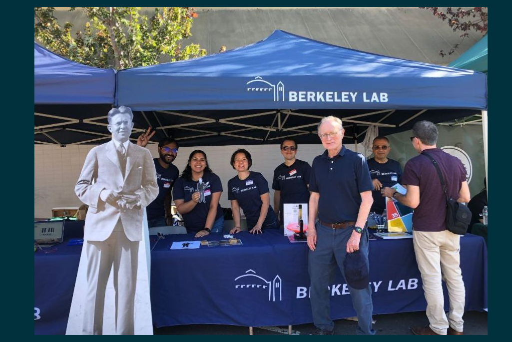 Persons standing in a Berkeley Lab-branded booth beside life-size cardboard cutout of founder, Ernest Lawrence.