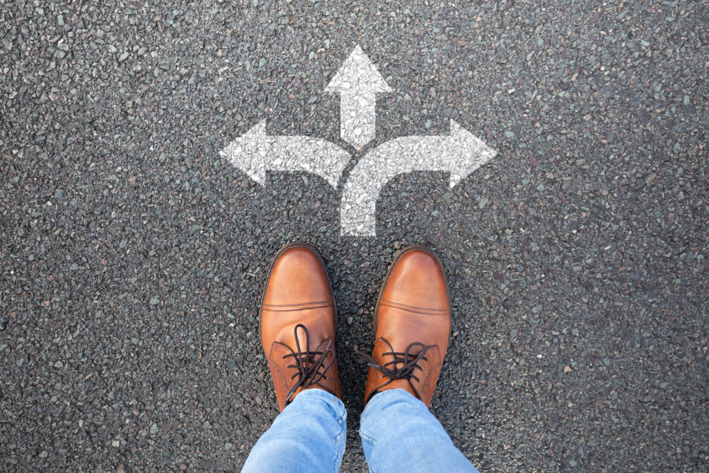 photo of a person's shoes on blacktop, standing in front of arrows pointing different directions