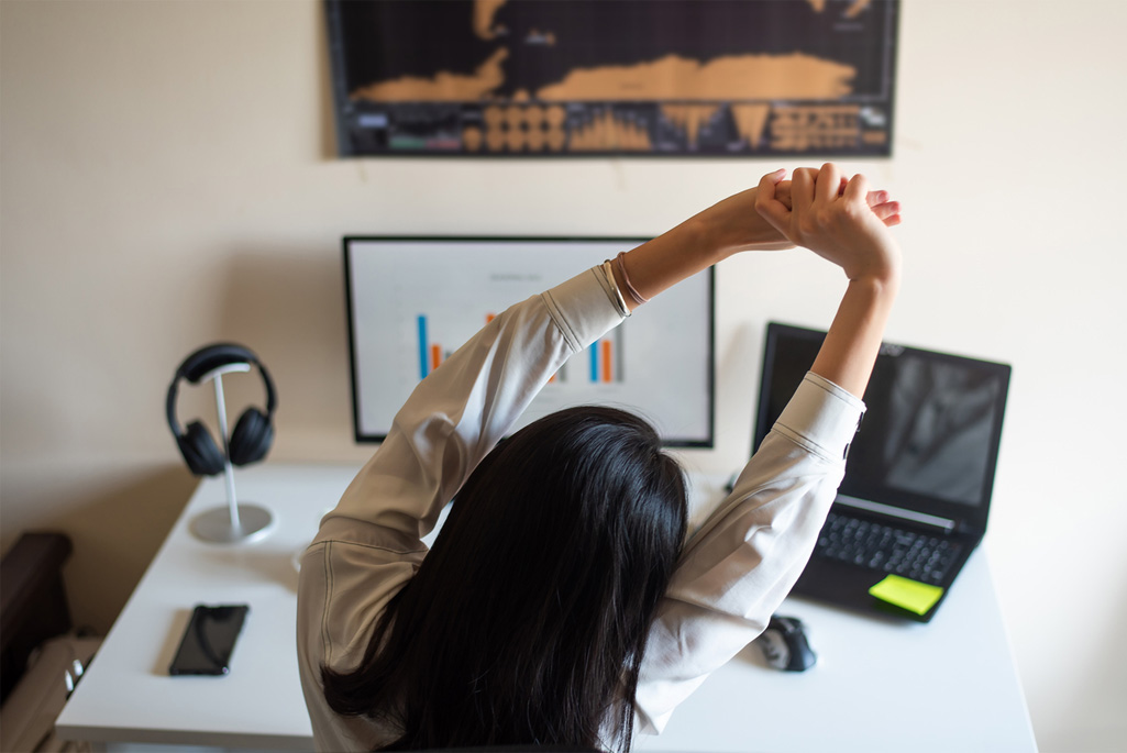 Woman stretching while working on computer from a home office.