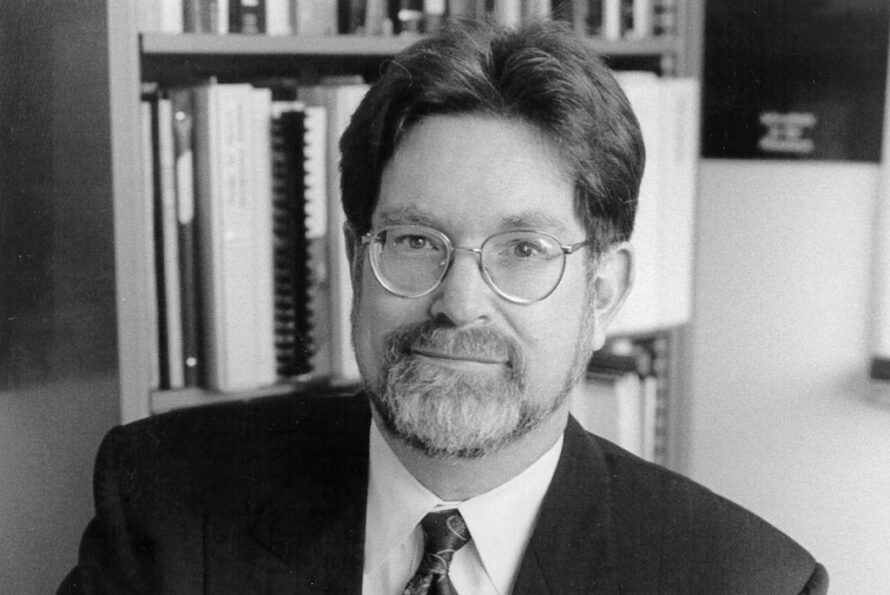 Black and white of person wearing suit jacket, tie, and wire frame glasses