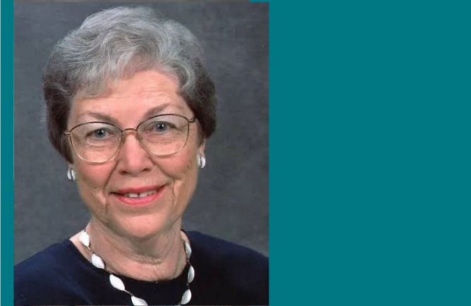 Headshot of person with short gray hair and wearing a black blouse with white necklace.