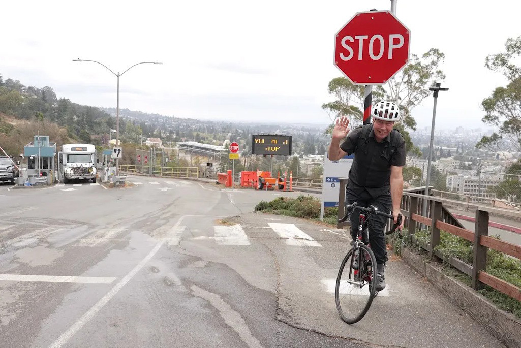 Cyclist on a bike at a stop sign wearing a helmet, waving.