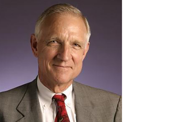 Person wearing suit jacket, white shirt, and red tie smiling looking into the camera