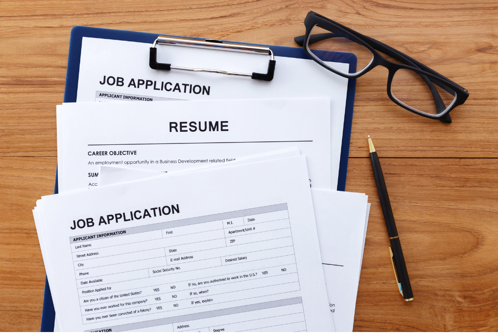 Closeup of applications on wooden desktop entitled "Job Application" and "Resume".