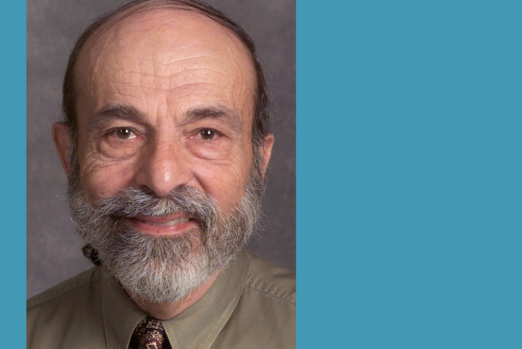 Headshot of person with gray beard wearing a brown shirt and necktie.