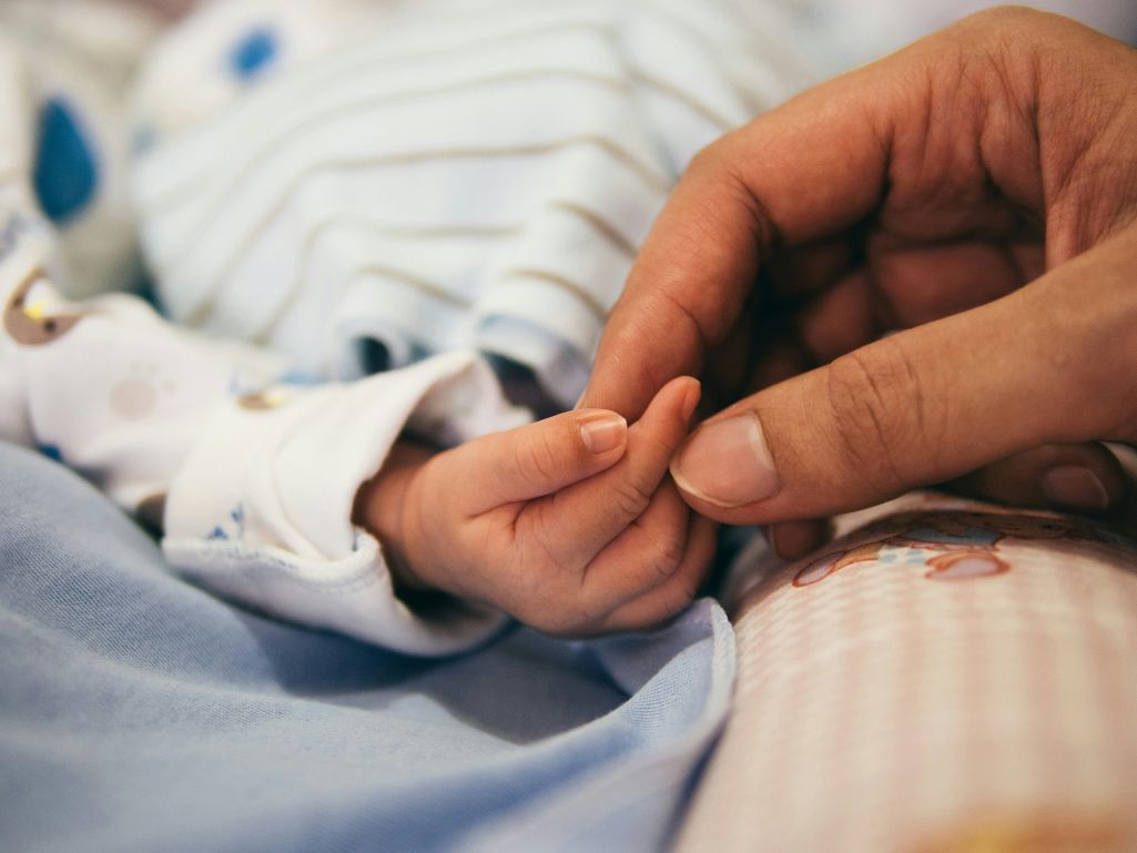 Close-up photo of Adult person's hands grasping an infant person's hand.