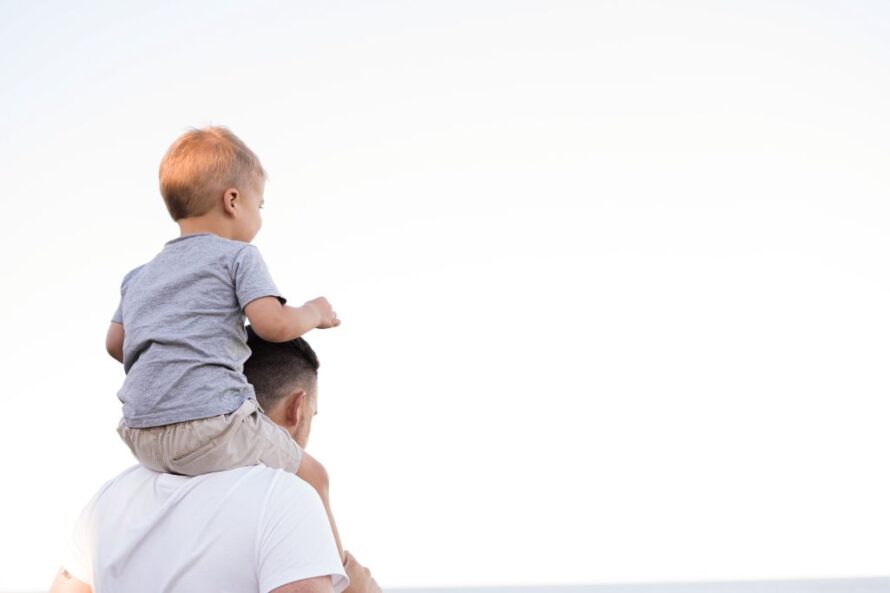 Photo of person with toddler riding on his back and both looking ahead.