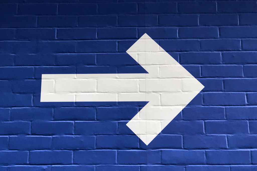 Blue brick wall with white right-pointing arrow in the middle of the wall.