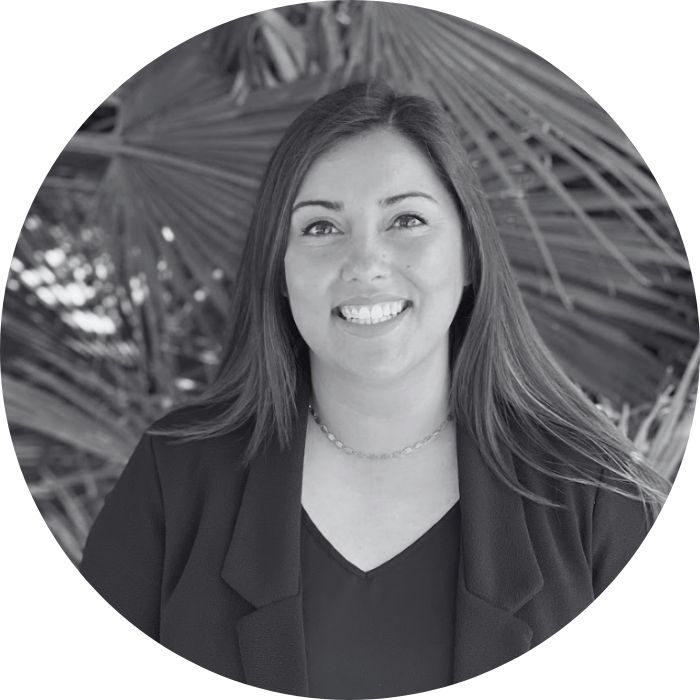 Black and white portrait of a person with long hair wearing a blazer and necklace, smiling.