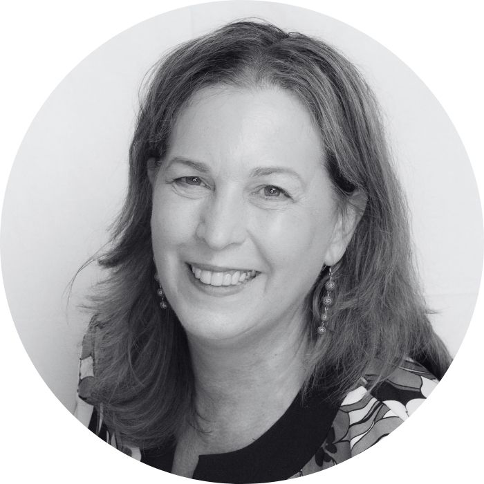 Black and white portrait of a person with long hair wearing a floral patterned top, smiling.