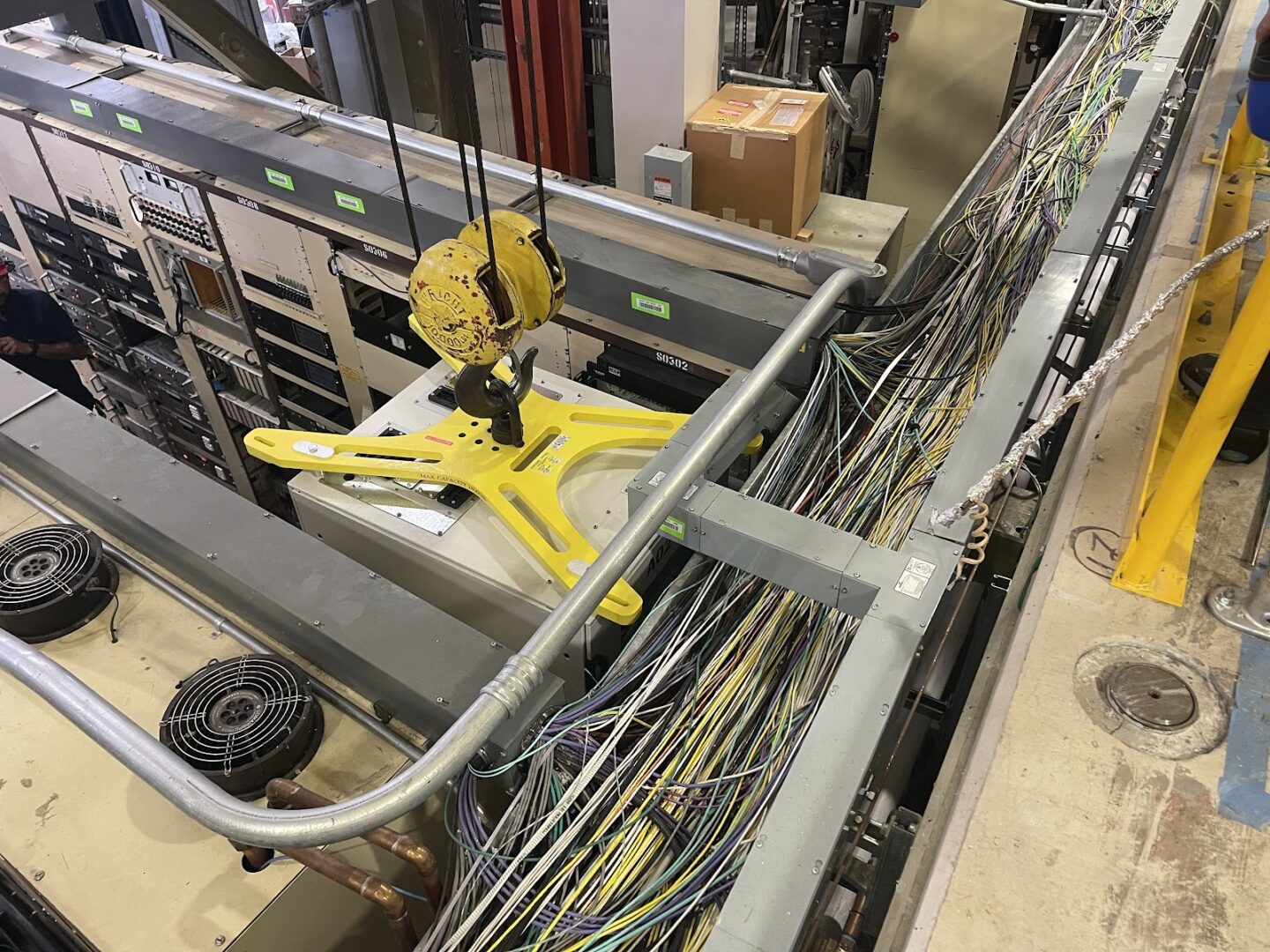 Up-close view of yellow, x-shaped rack lift fixture affixed to the top of a rack during a crane move in the ALS.