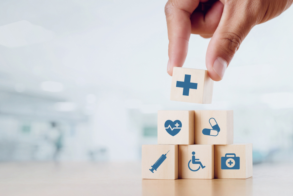 Image of a hand stacking blocks of icons related to health care