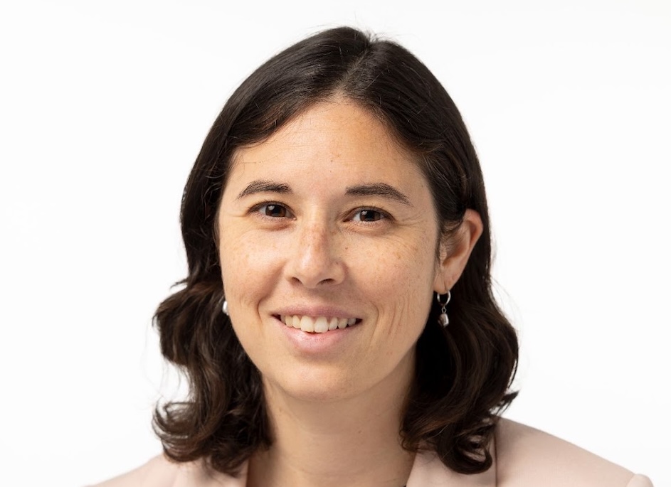 Headshot of person with shoulder-length, dark brown hair wearing earrings and smiling