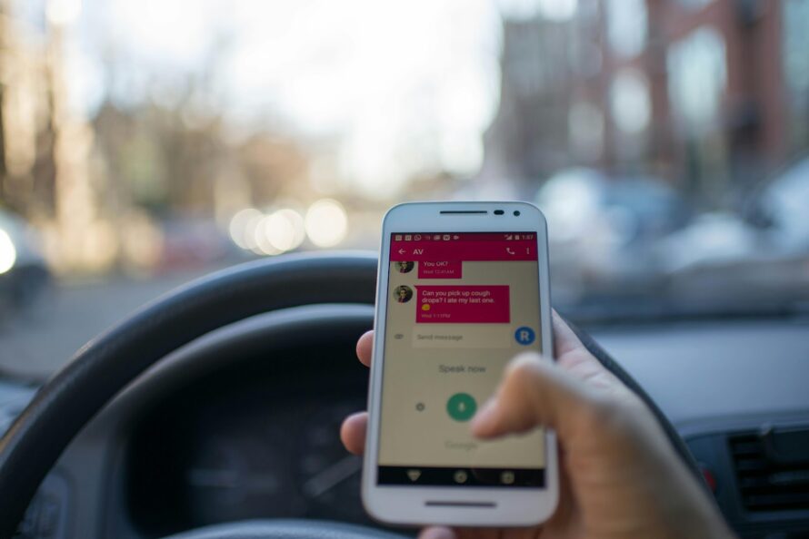 Closeup photo of person's thumb texting on phone that is resting on car's steering wheel