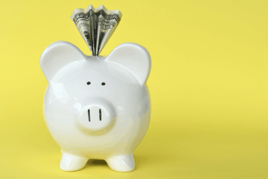 white ceramic piggy bank with dollar coming out of the top, against a yellow background