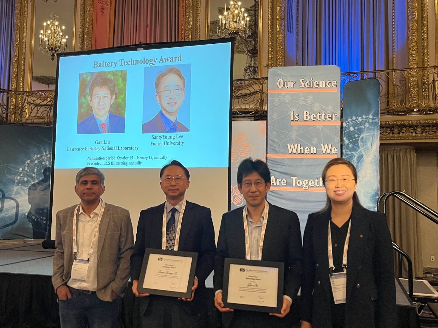 Four persons standing in line with the middle two holding award plaques.