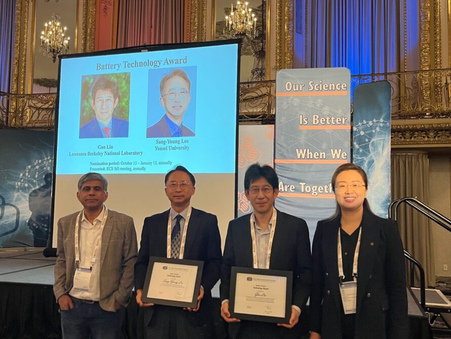 Four persons standing in line with the middle two holding award plaques.