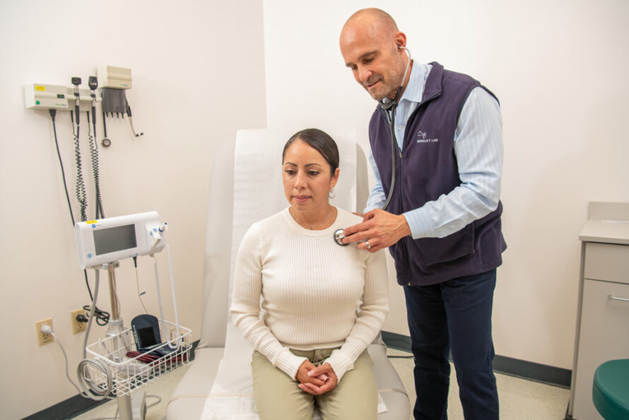 A medical director uses a stethoscope to check a patient’s health in a clinical examination room.