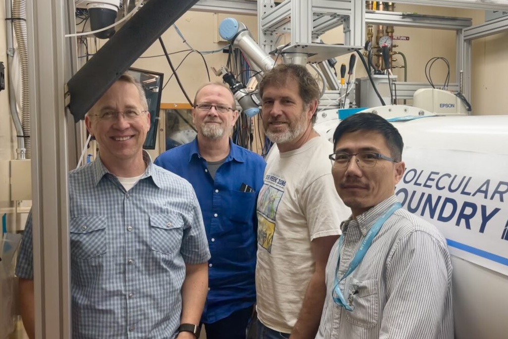 Four persons of the Berkeley Lab RADIUS robotics team stand next to robotics and automation features at Beamline 7.3.3