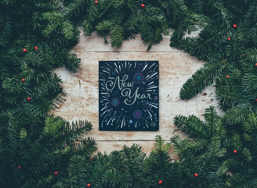 Photo of black chalkboard on wood surface with text "New Year" ringed by green foliage with red berries