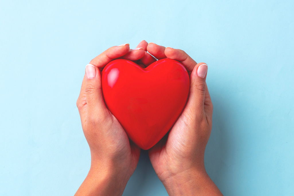 Two hands holding a heart-shaped item against a blue background.
