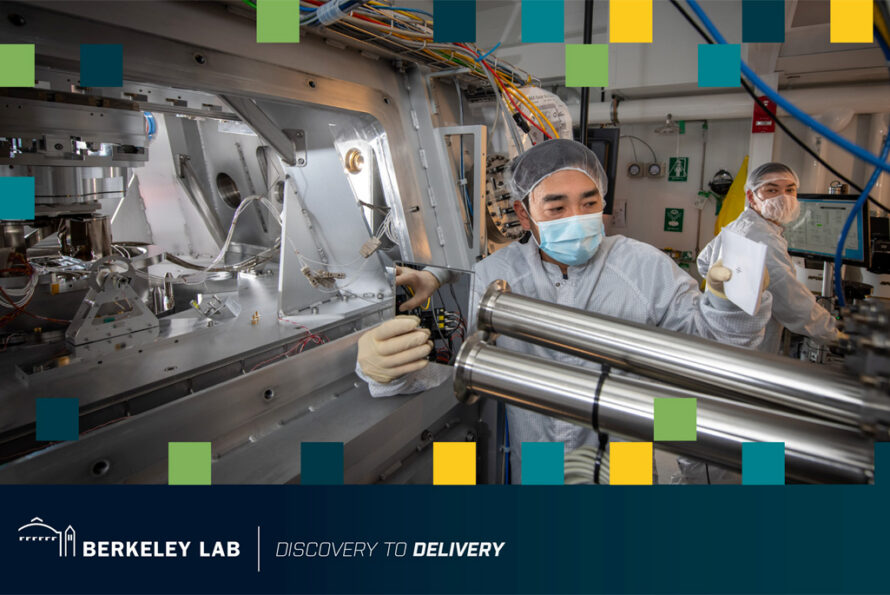 Two researchers wearing white lab coats in a lab with large metal machinery and blue cables.