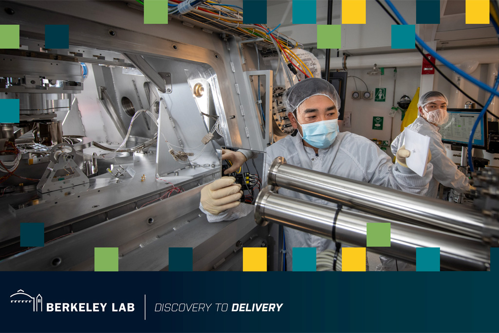 Two researchers wearing white lab coats in a lab with large metal machinery and blue cables.