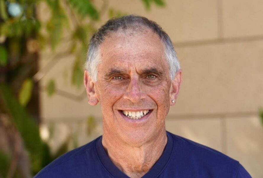 Head shot of person with short gray hair wearing dark blue v-neck shirt and smiling