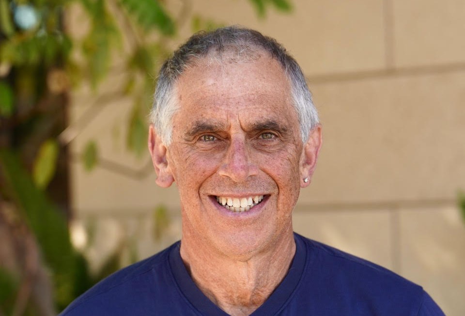 Head shot of person with short gray hair wearing dark blue v-neck shirt and smiling