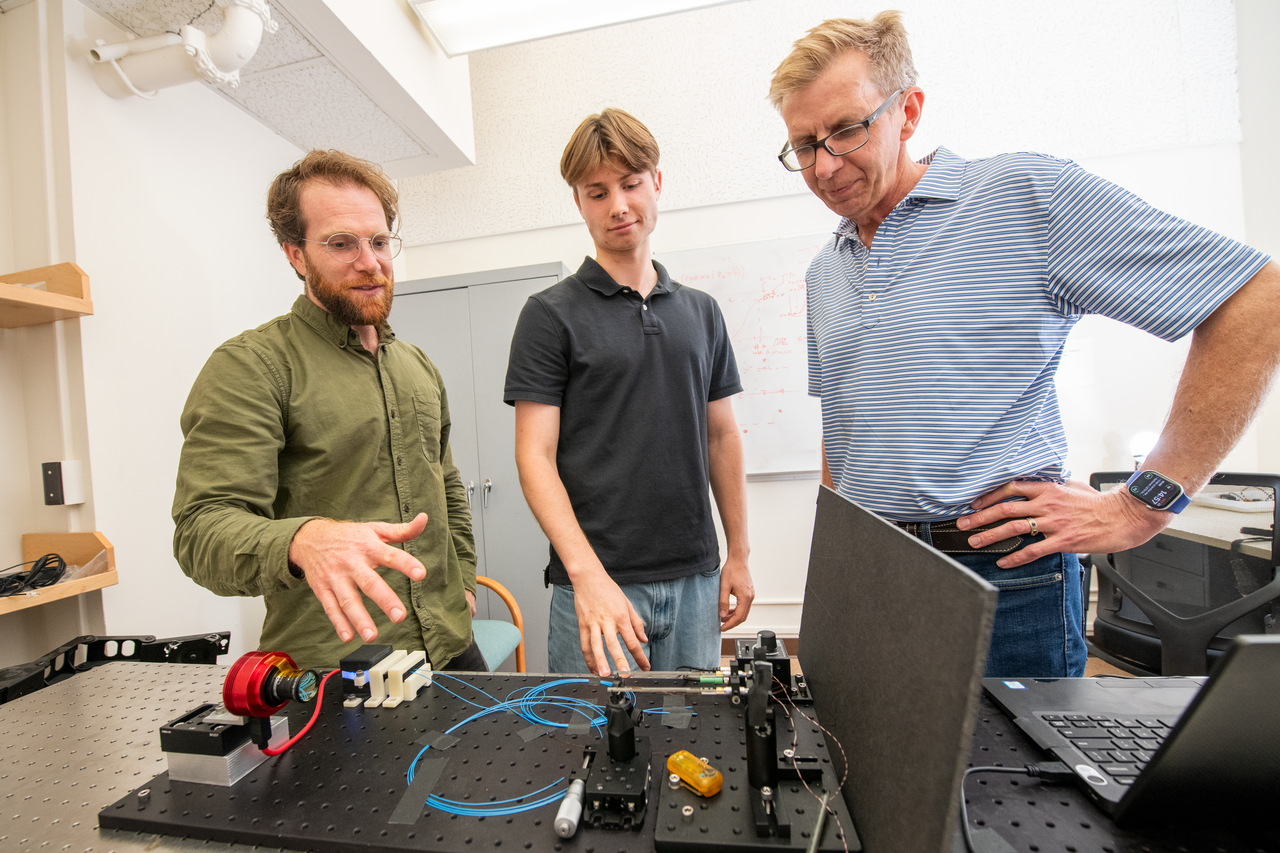 Three persons standing over a table looking down on scientific instrumentation
