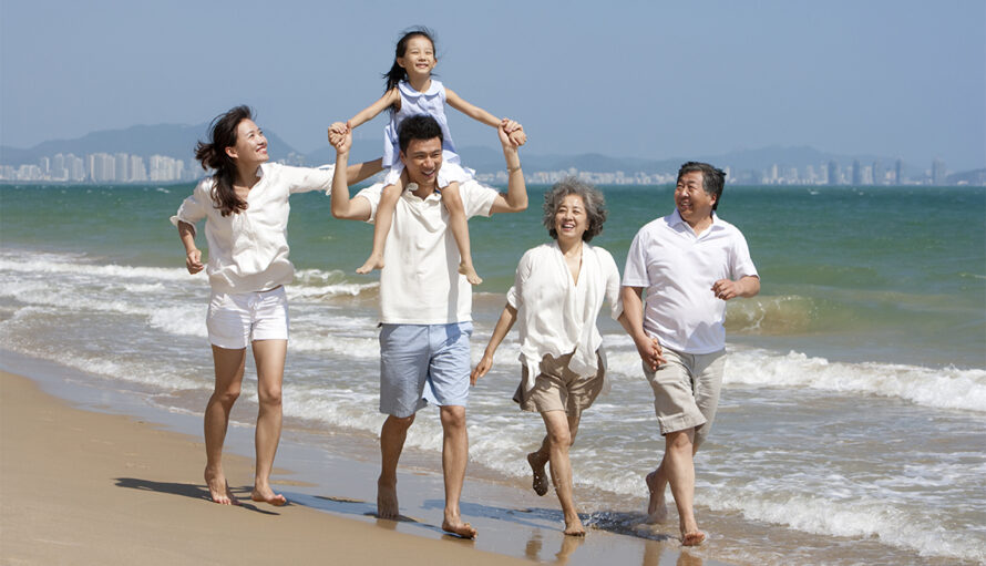 Five multi-generational family members wearing shorts and short-sleeved shirts walking together on a beach