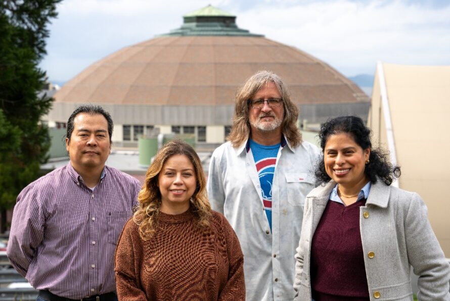 Four people standing outside for a photo, with the ALS in the background.