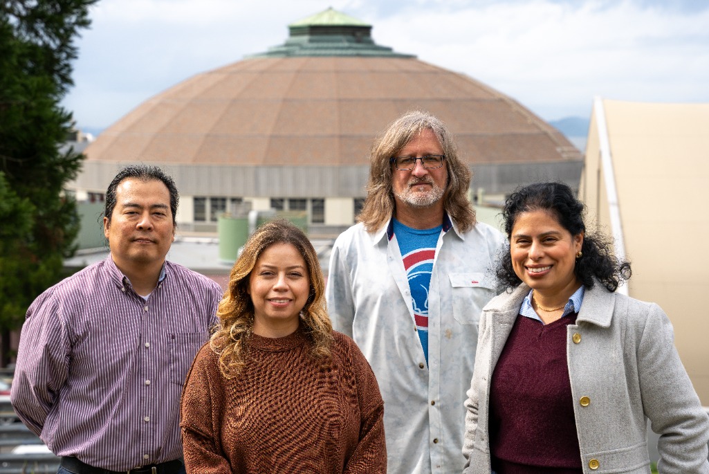 Four people standing outside for a photo, with the ALS in the background.