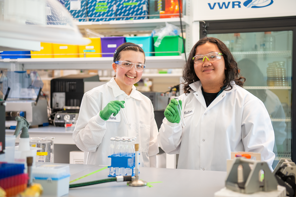 Two young people wearing white lab coats and holding beakers