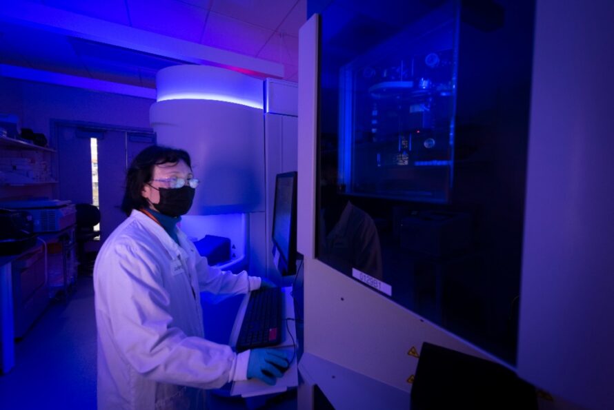 A researcher operates a robotic freezer system in a lab with dim purple lighting.