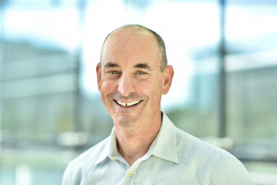Headshot of person with bald head wearing light green sport shirt and smiling