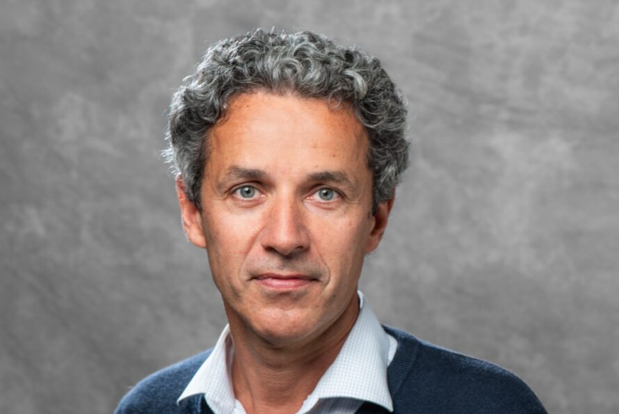 Headshot of person with gray and dark hair wearing dark blue sweater over a white business shirt