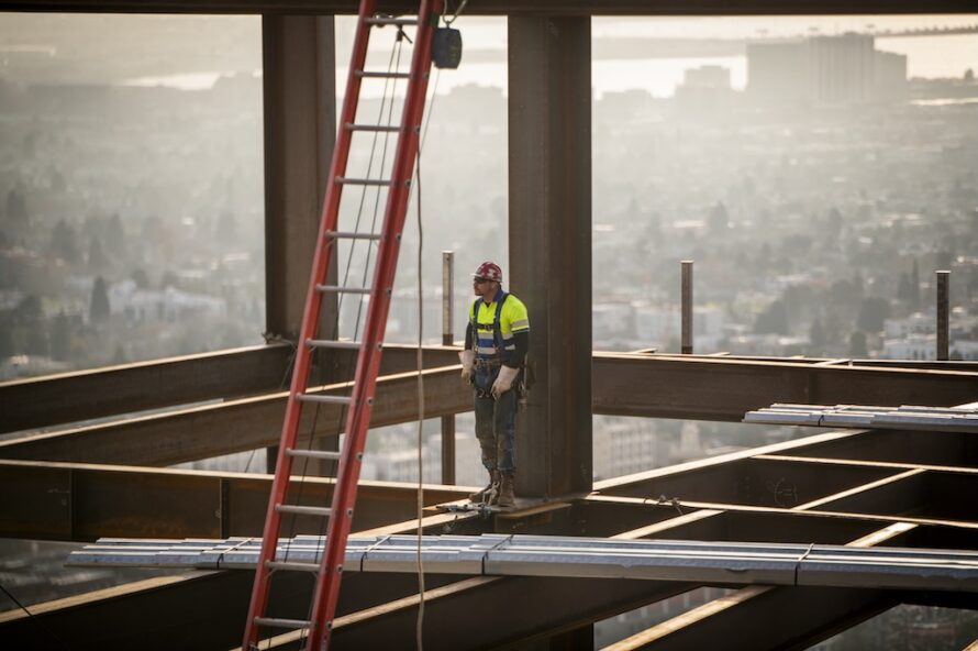 Construction worker standing on steel girder beam of Collaboration Commons building at Berkeley Lab with view of bay area in background