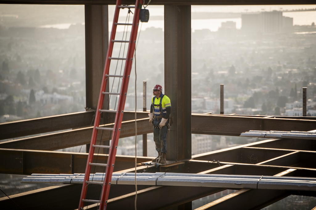 Construction worker standing on steel girder beam of Collaboration Commons building at Berkeley Lab with view of bay area in background