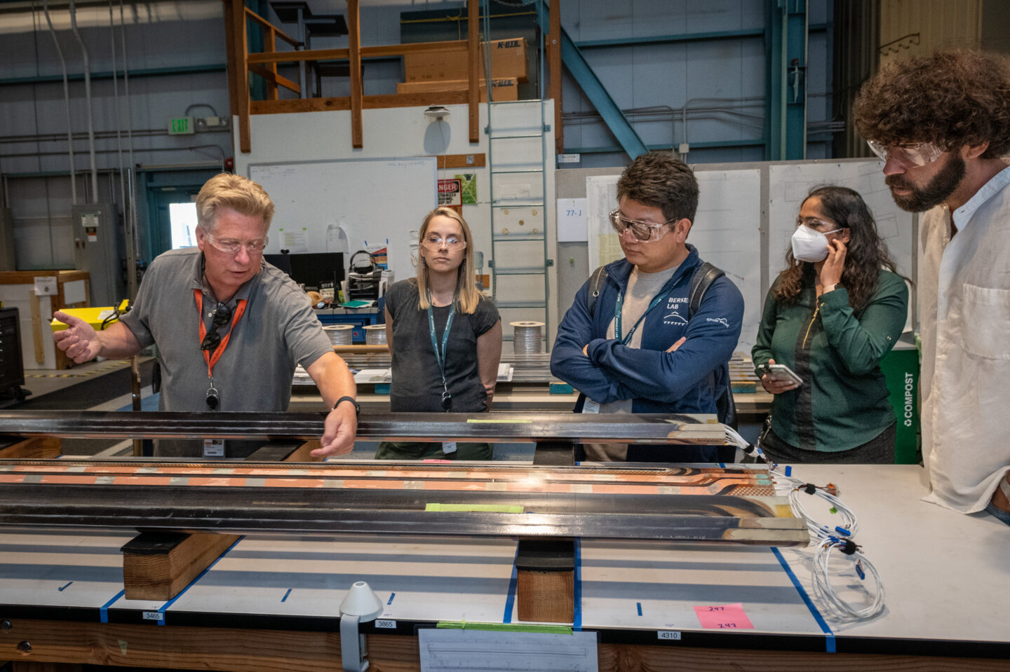 Five persons wearing protective eyewear and standing over a lab table while one person makes adjustments to instrument