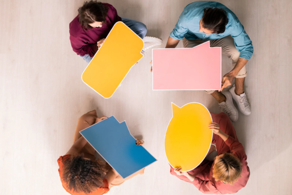 Aerial view of four seated persons with yellow, blue, and yellow thought balloons pointing towards each person
