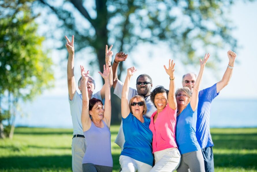 A group of adults with their arms raised in the air and are smiling while looking at the camera.