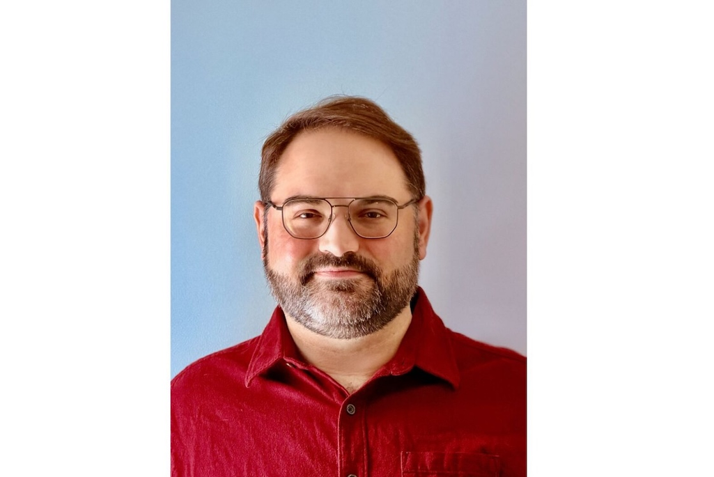 Headshot of person with short brown hair and a beard, wearing glasses and a red button-down shirt