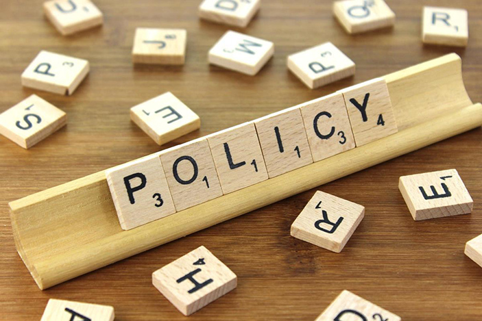 Six wooden tiles, each displaying a single letter, resting on a wooden stand that spell out the word "Policy"