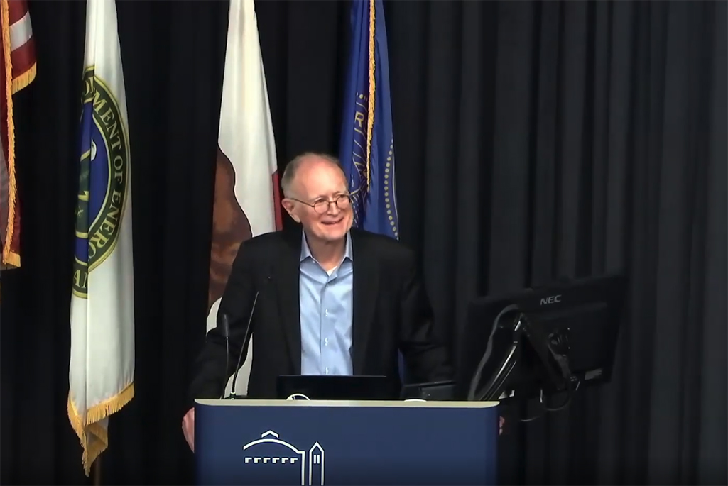 Person standing at podium wearing dark suit jacket and light blue shirt