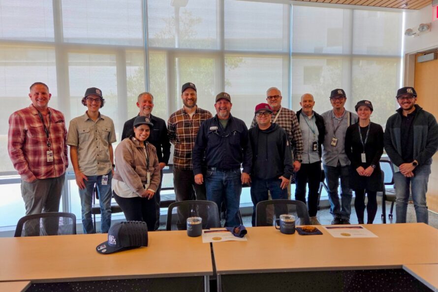 Group of persons standing in front of a conference table smiling with windows in background