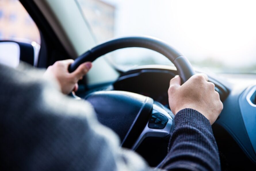 Close-up of person driving a car with both hands on steering wheel.
