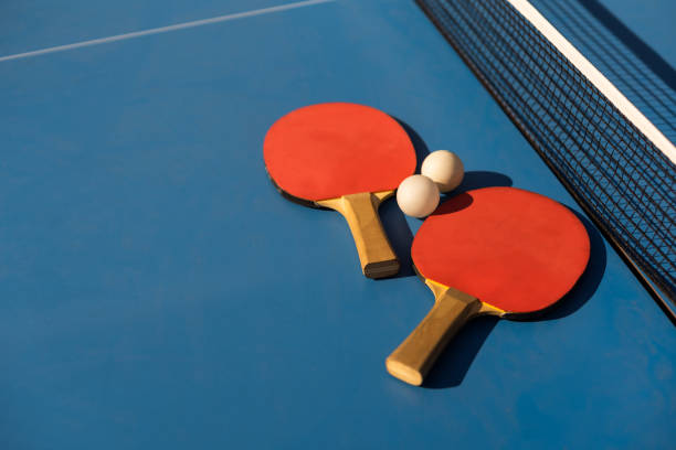 Closeup of blue ping pong table, net, and two red paddles and balls.