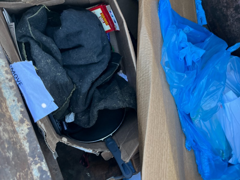 Discarded items in boxes. include clothing and a frying pan.