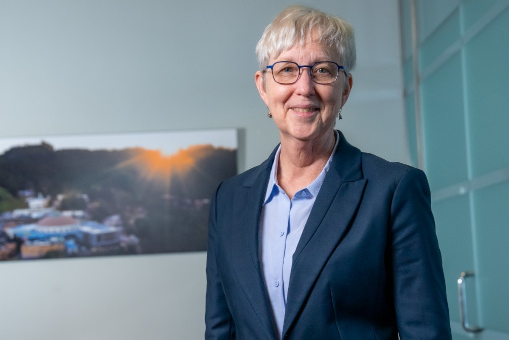 Katherine Yelick standing in front of an aerial image of Berkeley Lab.